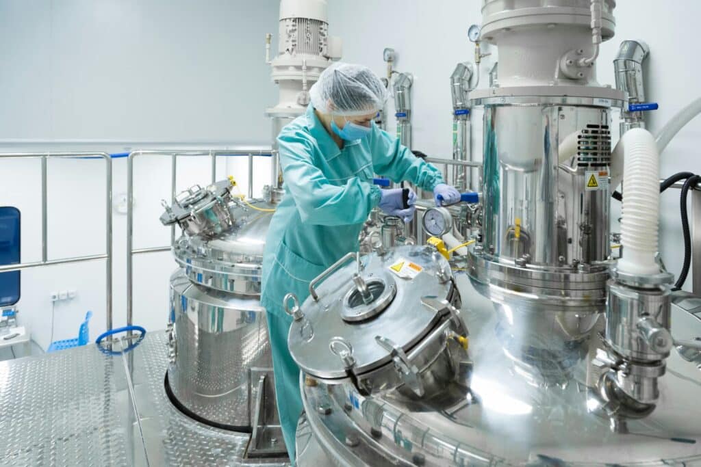 Technician in cleanroom attire operating stainless steel industrial processing equipment in a pharmaceutical or manufacturing facility