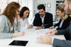 Team of professionals collaborating at a table, reviewing documents and discussing project details in a meeting.