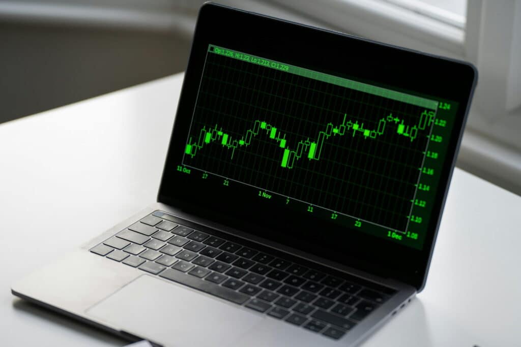 Laptop displaying a green candlestick stock chart on a dark screen, showing market price fluctuations over time.