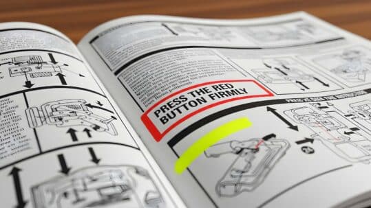 Close-up of an open instruction manual showing diagrams and step-by-step directions, with a highlighted section reading “Press the red button firmly” and arrows indicating movement.