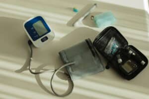 Blood pressure monitor with cuff, glucose meter kit, and medical supplies arranged on a light surface.