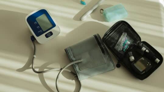 Blood pressure monitor with cuff, glucose meter kit, and medical supplies arranged on a light surface.