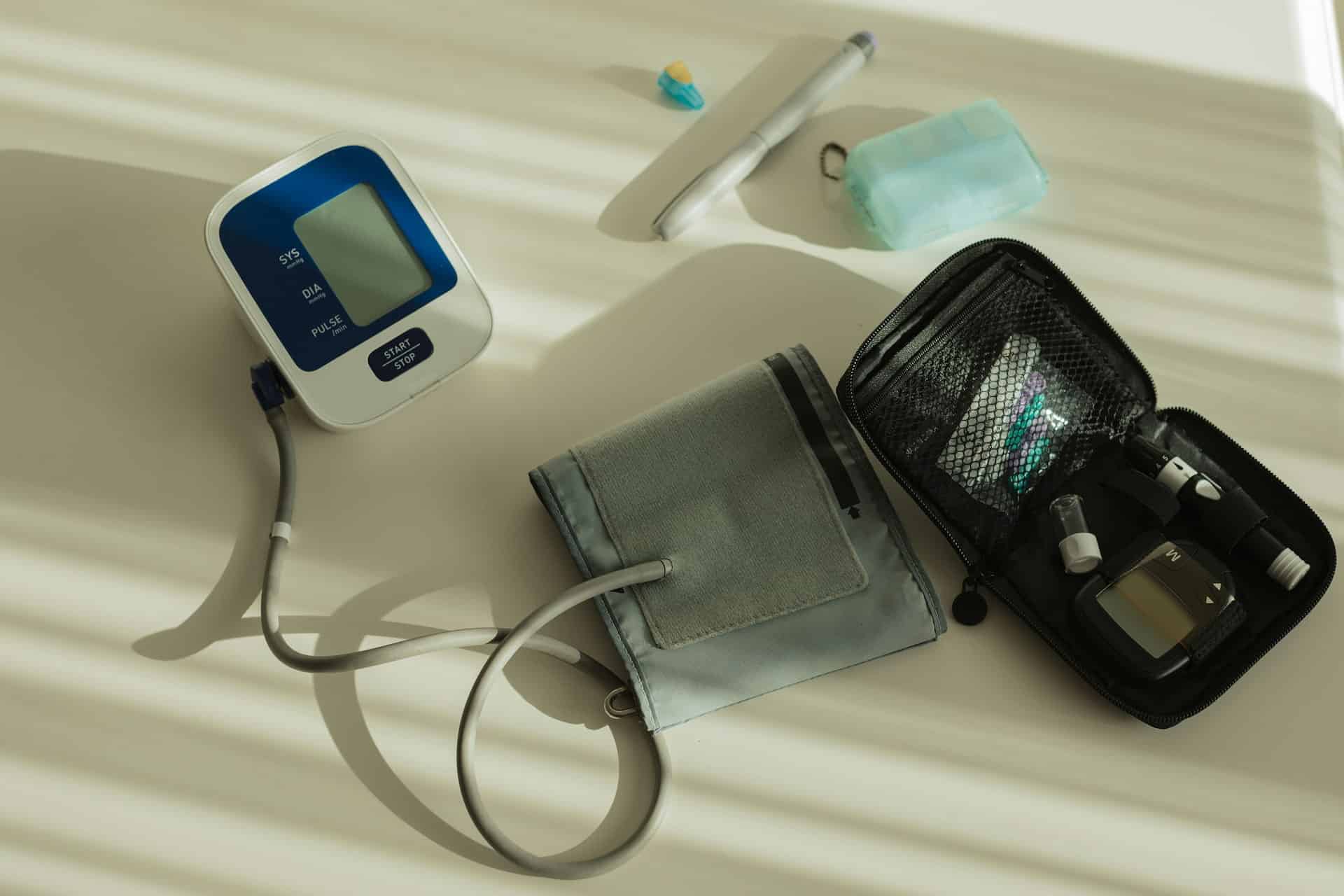 Blood pressure monitor with cuff, glucose meter kit, and medical supplies arranged on a light surface.