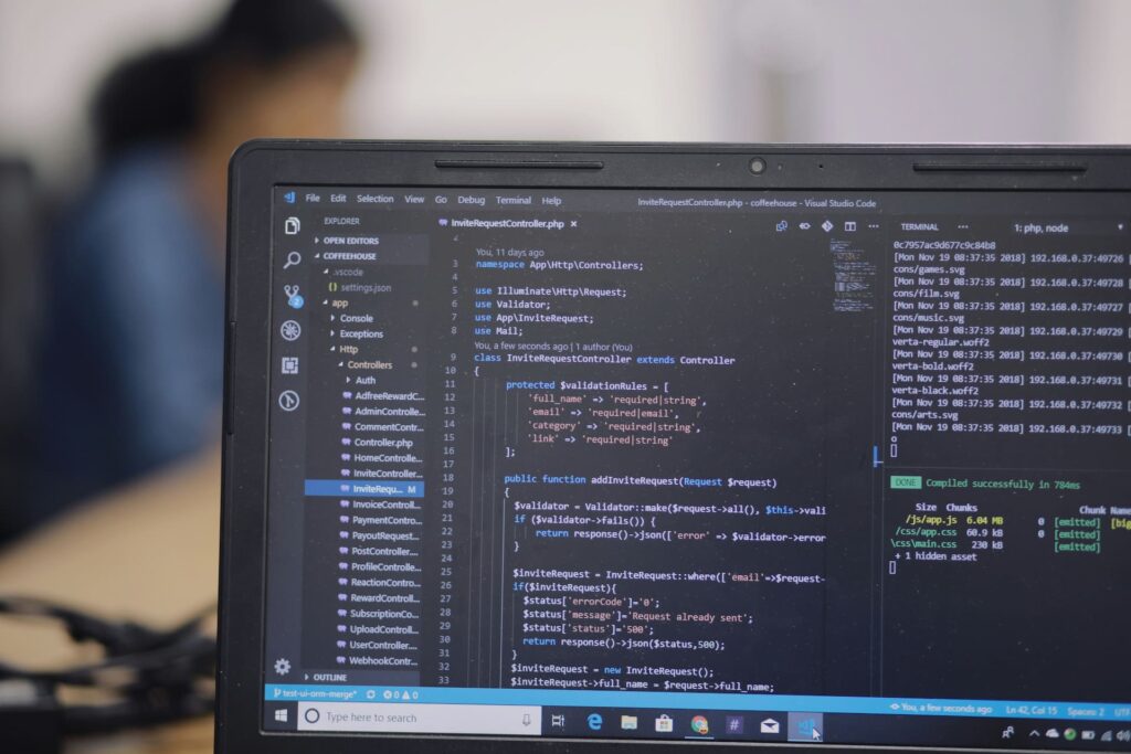 Close-up of a laptop screen displaying code in a development environment, with a blurred person working in the background.