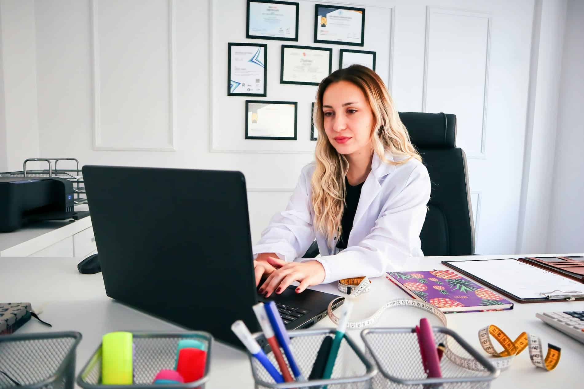 Healthcare professional reviewing documentation on a laptop in a medical office, illustrating healthcare technical writing, compliance, and documentation management.