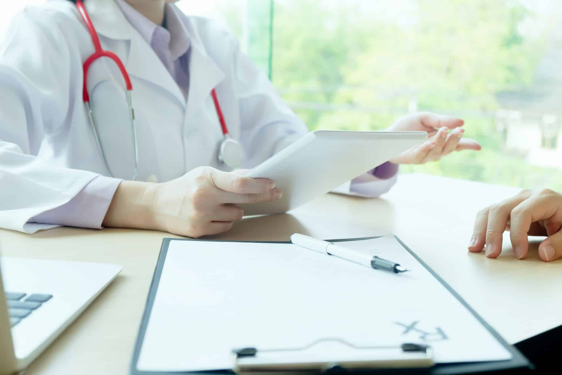 Healthcare professional reviewing medical documentation on a tablet while consulting with a patient in a clinical setting.