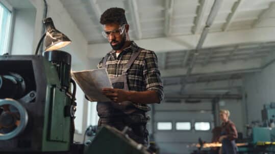 Manufacturing employee reviewing an SOP document beside industrial equipment