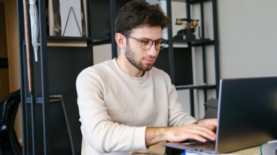 Technical writer working on a laptop in a modern office, creating documentation and technical content.