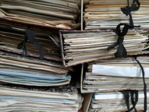Stacks of paper documents and folders illustrating disorganized technical documentation and record management.