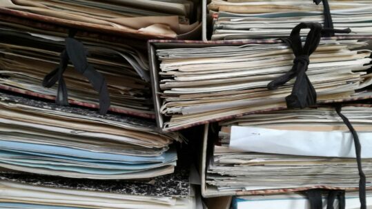 Stacks of paper documents and folders illustrating disorganized technical documentation and record management.