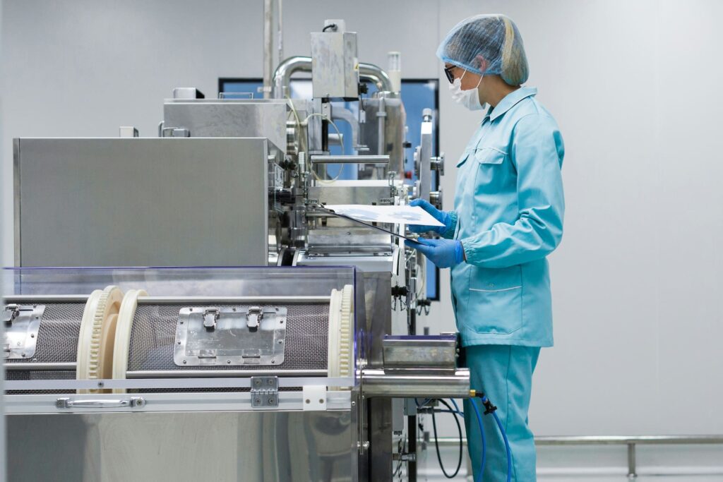 Quality assurance professional reviewing documentation beside pharmaceutical manufacturing equipment in a clean production facility.
