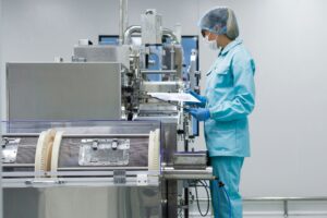 Quality assurance professional reviewing documentation beside pharmaceutical manufacturing equipment in a clean production facility.