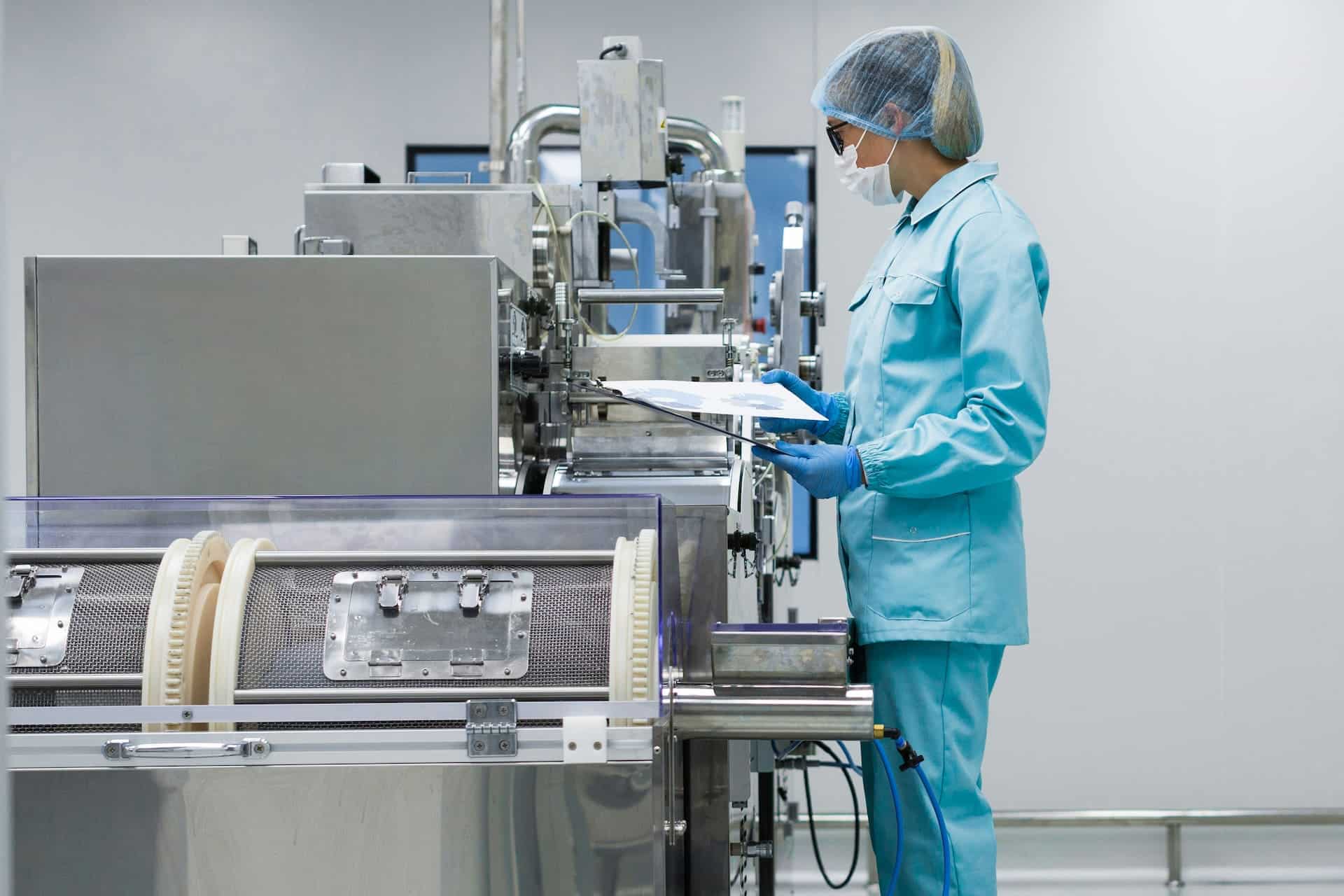 Quality assurance professional reviewing documentation beside pharmaceutical manufacturing equipment in a clean production facility.
