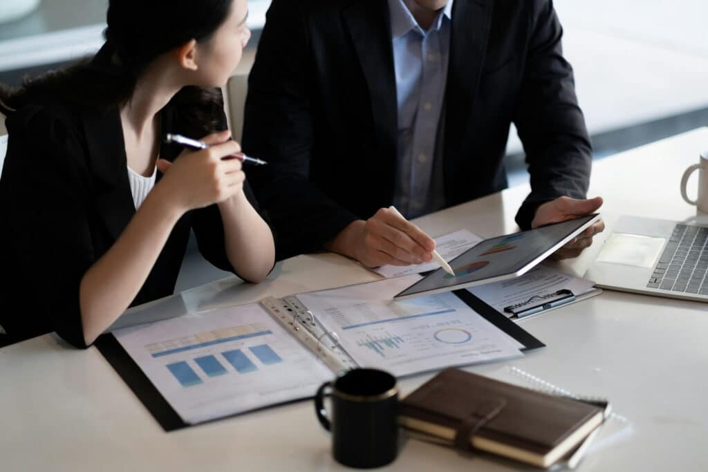 Business professionals reviewing resource planning data and performance charts on a tablet during a meeting.