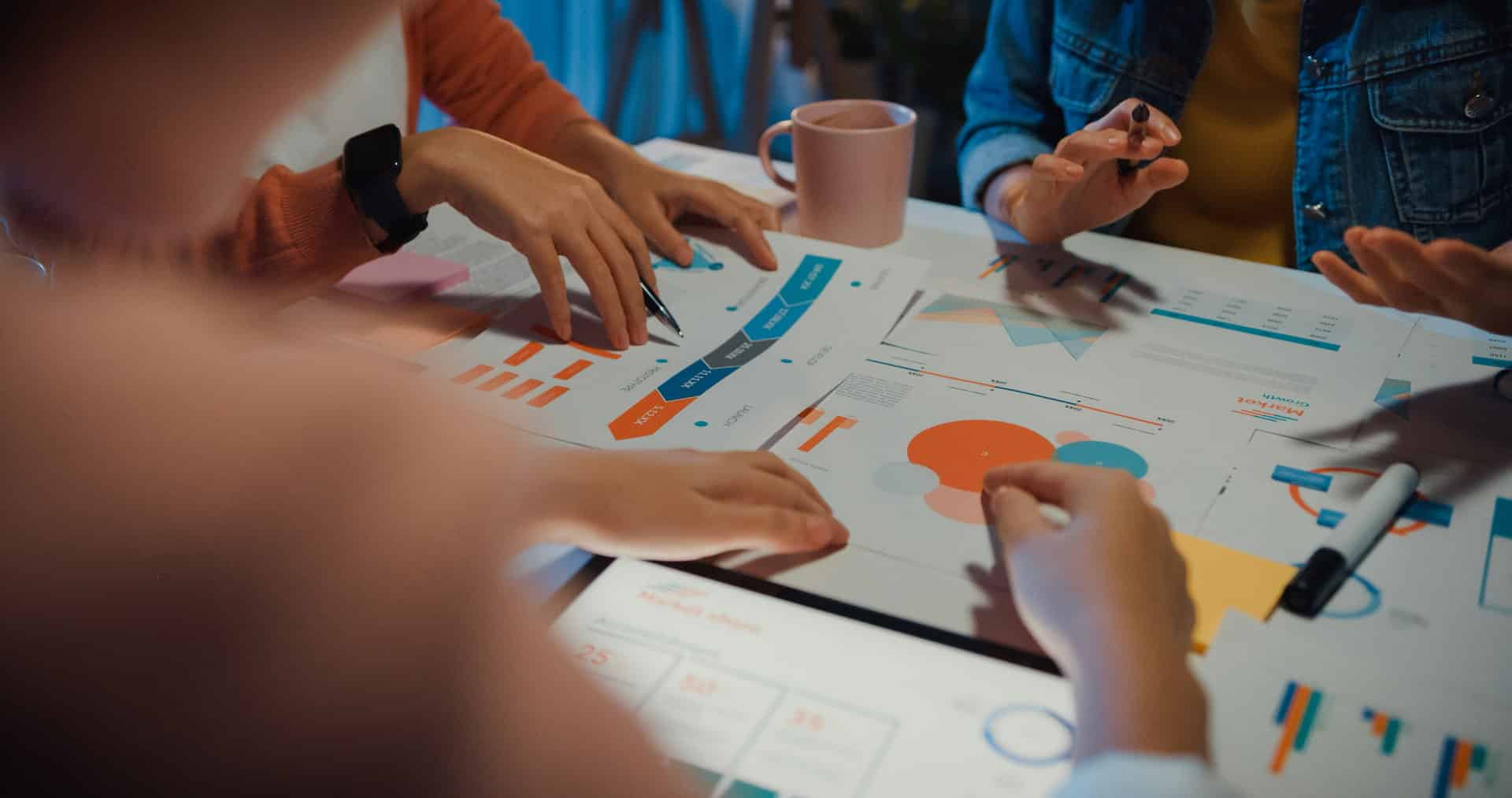 Marketing team collaborating around a table with charts, graphs, and data reports during a strategy discussion.