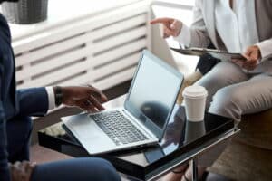 Two business professionals reviewing documents and discussing information beside an open laptop during a meeting.