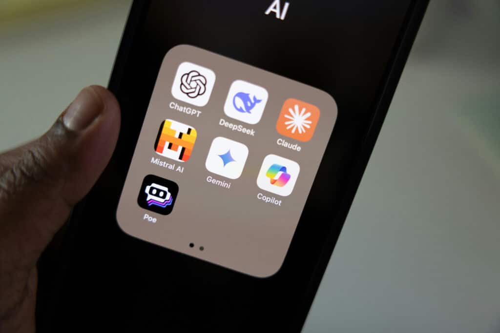 Close-up of a smartphone displaying a folder of popular AI apps, including ChatGPT, DeepSeek, Claude, Mistral AI, Gemini, Copilot, and Poe.