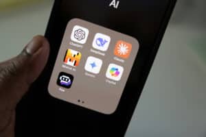Close-up of a smartphone displaying a folder of popular AI apps, including ChatGPT, DeepSeek, Claude, Mistral AI, Gemini, Copilot, and Poe.