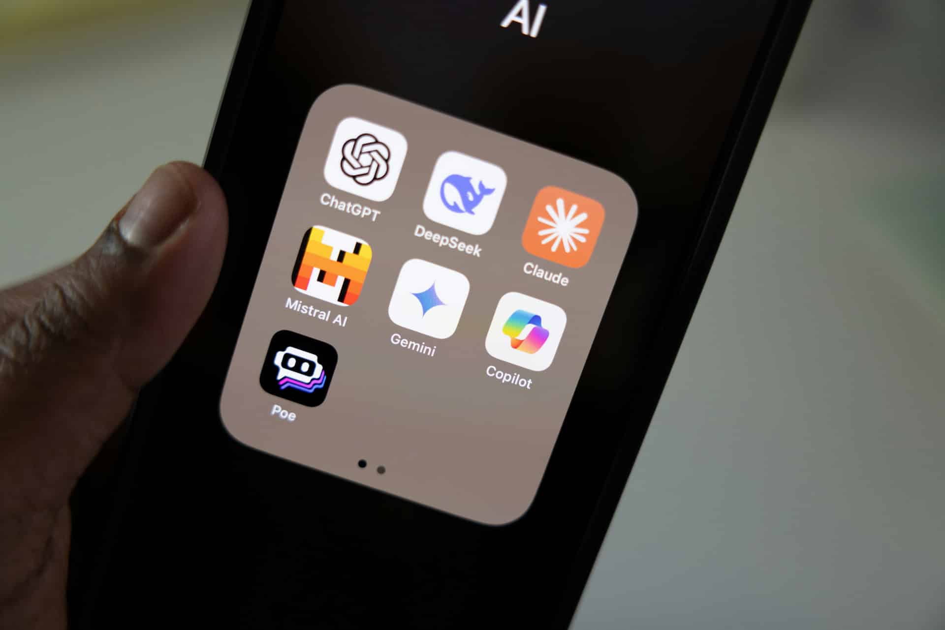 Close-up of a smartphone displaying a folder of popular AI apps, including ChatGPT, DeepSeek, Claude, Mistral AI, Gemini, Copilot, and Poe.