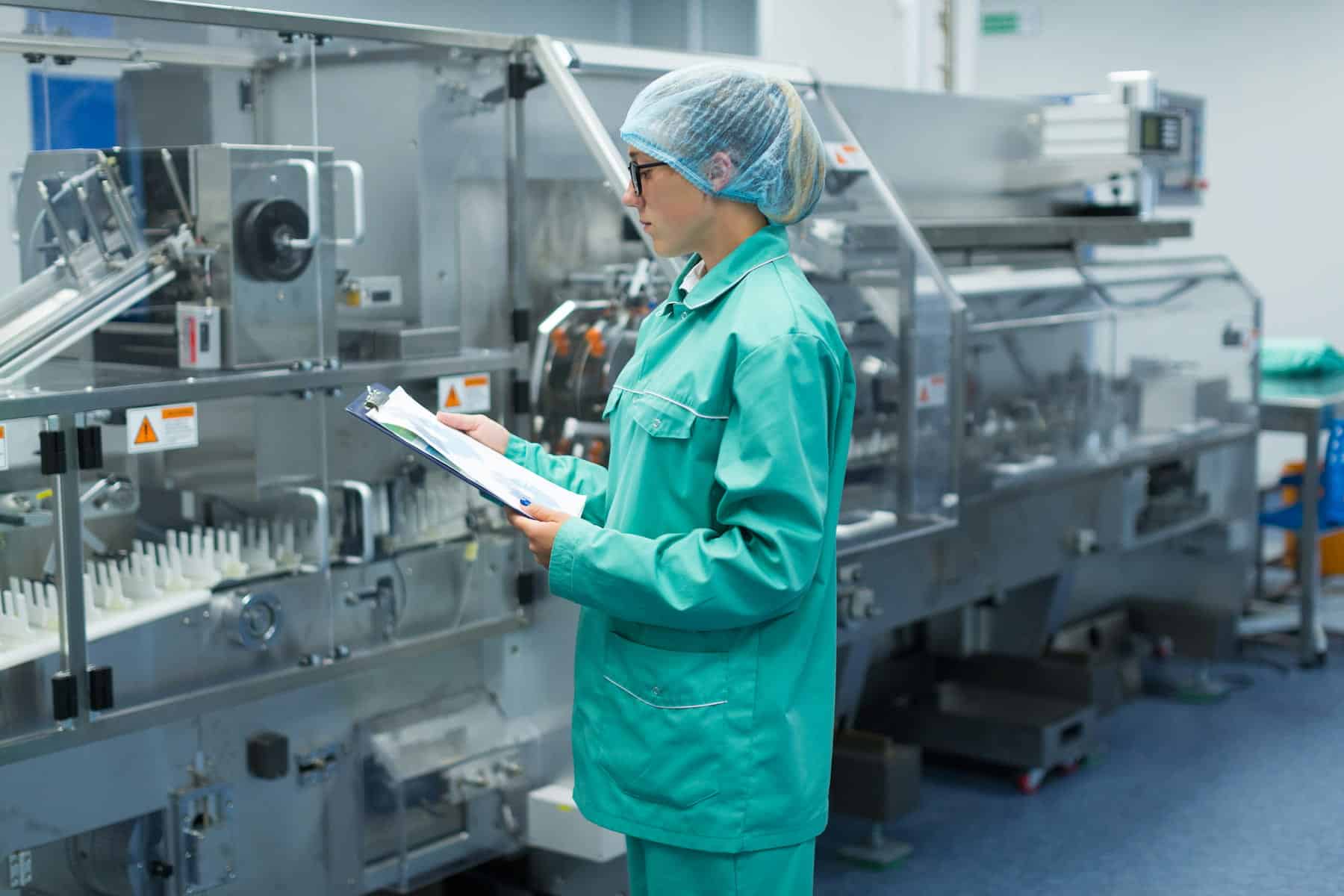 Worker in a hairnet reviews paperwork beside an automated production line.